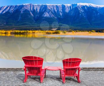 Two red comfortable loungers by the Abraham lake. Warm September in the mountains of Canada. Concept of ecological and active tourism