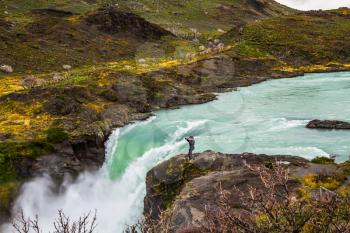 Travel to Patagonia. A lonely woman photographer on a cliff near the powerful waterfall Salto Grande in Torres del Paine. Concept of active and extreme tourism