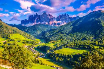  The sun illuminates grandiose crenellated rocks of Tirol. Small picturesque village in Alpine meadows. The Dolomites. The concept of eco-tourism