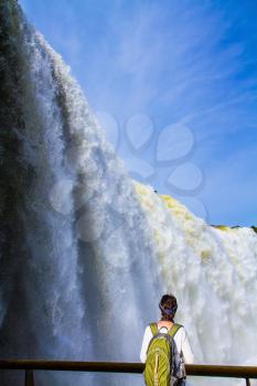 Elderly tourist woman with a backpack watching the waterfall. The world of roaring water. Iguazu Falls in South America. Concept of active and extreme tourism