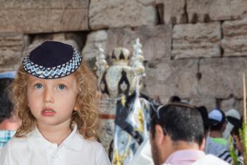 Handsome little boy with blond side curls and blue eyes, in skullcap. Western Wall of the Temple. Autumn Jewish holiday Sukkot. The Jews brought the Torah Scroll for prayer