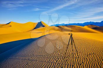 Tripod with camera stands on sand dune. Mesquite Flat Sand Dunes. Bizarre twists of orange sand dunes 