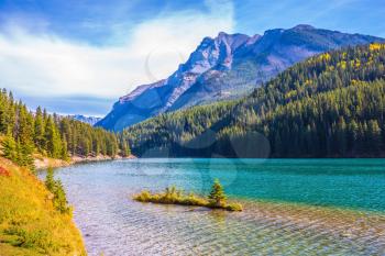 The Magnificent Lake Two Jack. The pure turquoise water of the lake reflects coniferous forests. A charming little island near the shore. The concept of ecological and active tourism