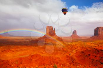 Huge balloon flies over Red Desert Navajo, USA. The picturesque rainbow crosses some rocks - mitts