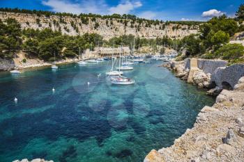 Picturesque narrow fjords between stony coast. White sailing yachts wait for the owners.  National Park Calanques on the Mediterranean coast