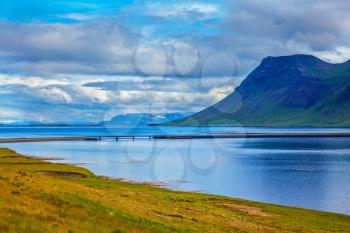 Smooth water of the cold fjord reflects clouds. Cold summer in Iceland