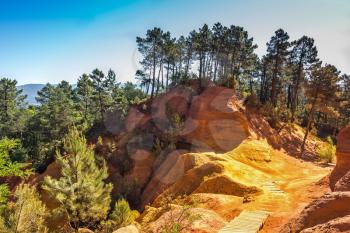 Beautiful and striking contrast between the green pine trees and yellow ocher soil. Unique red and orange hills in the province of Languedoc - Roussillon, France