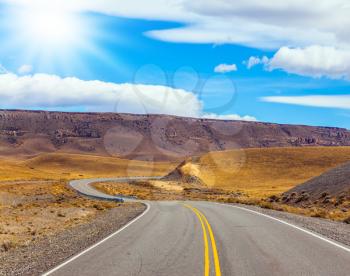 Asphalt road in the Argentine prairie. Patagonia. Summer day in February. The concept of active and extreme tourism. The summer sun illuminates the prairie