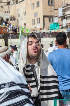 JERUSALEM, ISRAEL - OCTOBER 12, 2014: The area in front of Western Wall of  Temple filled with people.  Morning autumn Sukkot. The young guy in tallit prays