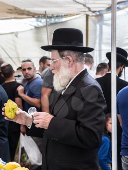 JERUSALEM, ISRAEL - OKTOBER 16, 2016: Traditional market before the holiday of Sukkot. Elderly ortodox Jew with white beard is checking with lupa ritual plant etrog - citrus