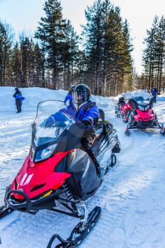 Snowmobiling. Tourist train from snowmobiles moves along the ice of a frozen river. Concept of active winter tourism