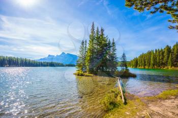 Lake Two Jack in the Rocky Mountains. The morning sun warms the lake and a small island. Golden Autumn in Canada. The concept of ecological and active touris