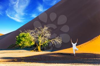 The concept of extreme and exotic tourism. Purple and yellow dune of the Namib desert. An elderly woman practicing yoga in the desert