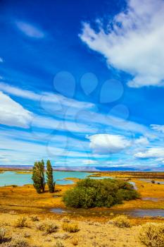  The concept of active and exotic tourism. Flat plain with shallow lakes and yellowed grass. Patagonian Pampas. Strong wind carries clouds