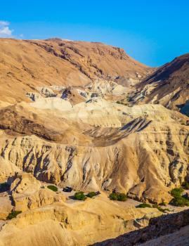 The concept of extreme tourism. Bright hot summer day. Dry ancient mountains in the vicinity of the Dead Sea. At the bottom of the canyon are several green trees