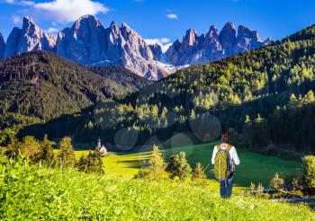 Woman-tourist with backpack admire nature. Sunny day in Dolomites, Tirol. Forested mountains surrounded by green Alpine meadows. The concept of an active and eco-tourism