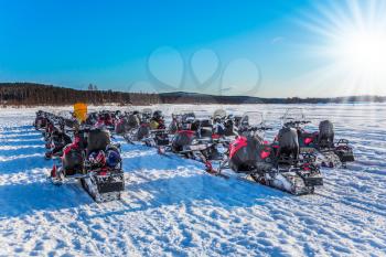 Concept of active winter tourism. Tourist train from snowmobiles moves along the ice of a frozen river. Snowmobiling