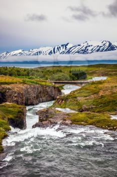 The rapid creek flows among the flat tundra. The concept of extreme northern tourism. On the horizon - rhyolite mountains in the snow