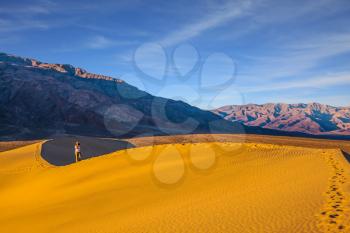Woman in striped shirt photographing sand waves. Mesquite Flat Sand Dunes. Bright sunny morning in a picturesque part of Death Valley, USA