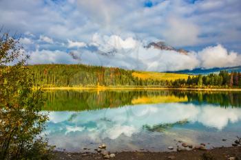 Warm autumn day in park Jasper, the Rocky Mountains of Canada. Charming Patricia lake among evergreen forests, yellow bushes and far mountains