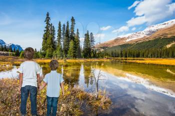 Two boys standing on the shore of a shallow lake. Rocky Mountains on a sunny autumn day. The concept of active tourism