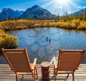 Two comfortable wooden chairs and a small round table on the lake. Indian summer in the Rocky Mountains of Canada. Concept of ecological tourism