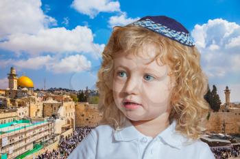 Little boy with long blond curls and blue eyes. Adorable Jewish child in a blue skullcap. Jerusalem, Western Wall of Temple  