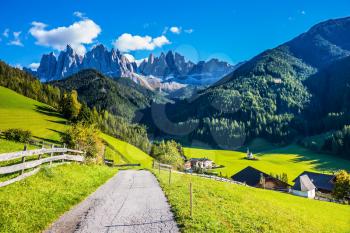 The road descends into the valley. Warm autumn in the Dolomites. The concept of ecological tourism. Rocky peaks and forested mountains surrounded by green Alpine meadows 