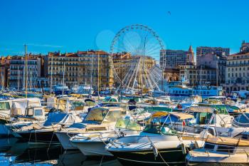 The water area of Marseille Old Port. On the waterfront - a huge Ferris wheel. Rows of white sailing yachts, motor boats and fishing boats