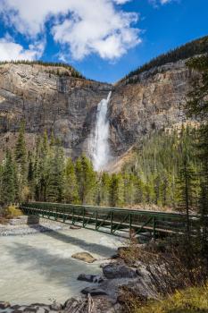 Waterfall Takakkaw in Yoho National Park in the Rocky Mountains. Small footbridge across the turbulent river