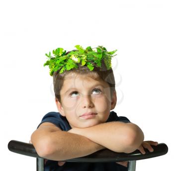 Very beautiful seven year old boy in a carnival wearing a crown of shiny green leaves. He sits astride a chair