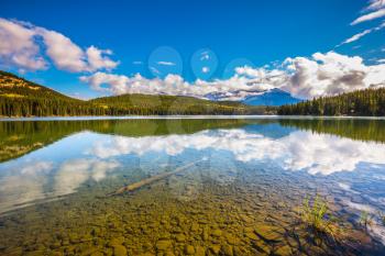 Clear water Pyramid Lake reflects the clouds and pine forests on shore. Frosty morning in the Rocky Mountains, Canada