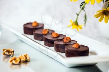 Gorgeous confectionery desserts. Portion small chocolate cakes are decorated with nuts. Background - a white vase with field chamomiles