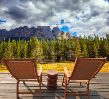  The lush  autumn in Rocky Mountains of Canada. On the wooden platform there are two wicker deck chairs
