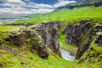 The striking canyon in Iceland. The concept of active northern tourism. Bizarre shape of cliffs surround the stream with glacial water. Green Tundra in July