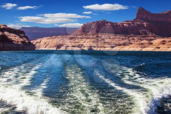  Foamy trace of a motor boat crosses the emerald waters. Red sandstone hills surround the lake. Lake Powell on the Colorado River
