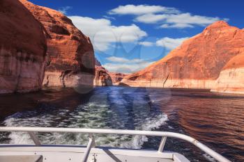 Lake Powell on the Colorado River. Walk on the tourist boat. Foam boat trail crosses the emerald waters. Red sandstone hills surround the lake