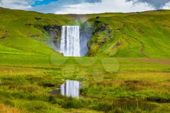 Grandiose reflection. The huge deep falls Skogafoss are reflected in small stream