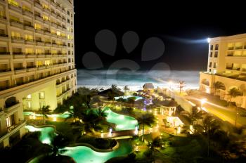 Beach front hotel at night with swimming pools in the foreground and the ocean in the back