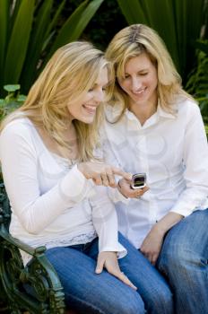 Royalty Free Photo of Women on a Park Bench Looking at a Camera Phone