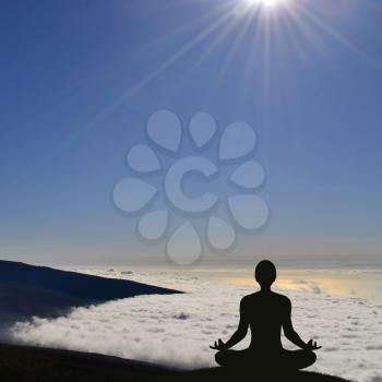 Silhouette of a yogi in lotus pose above clouds