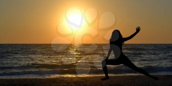 Woman silhouette in a yoga pose on the beach at sunrise