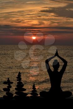 Silhouette of woman in yoga posture and balanced stones at sunrise