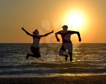 Two friends jumping on beach during sunrise