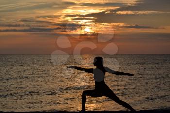 Woman practicing yoga, standing in  pose at sunrise