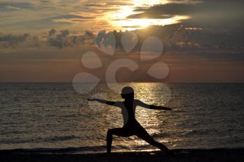 Woman practicing yoga, standing in Virabhadrasana pose at sunset