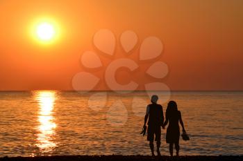 Back view of a couple silhouette walking together on the beach at sunrise in summer