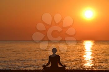 Yoga silhouette of a man sitting in lotus pose against the background of the sea and sunrise