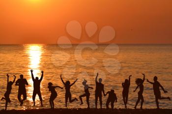 Men and women jumping and enjoying life at sunrise on the beach