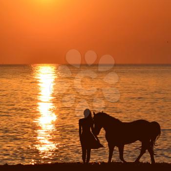 Woman with a horse at sunrise on the sea shore